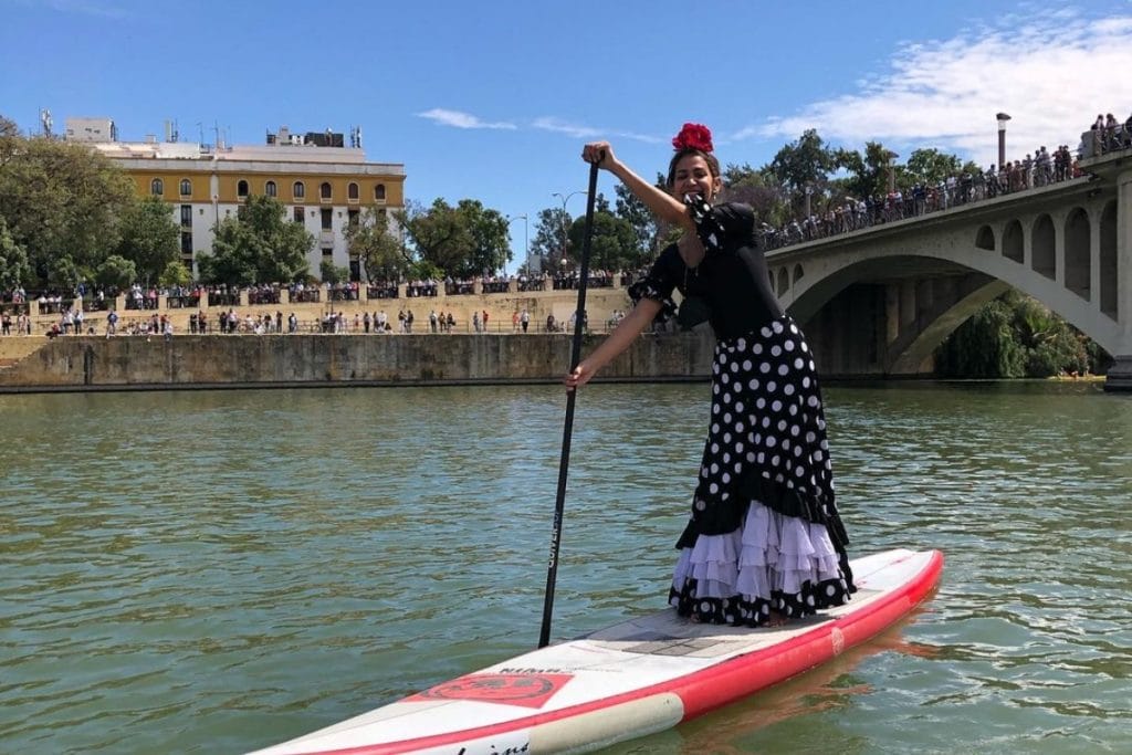 Una mujer vestida de flamenca recorre el Guadalquivir haciendo paddle surf