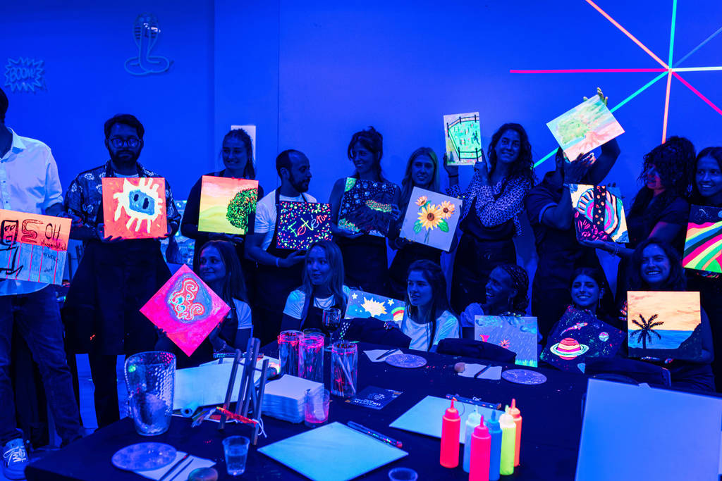 Group of people showing their works created with neon paints in the dark.
